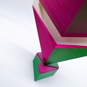 May include: A set of three geometric wooden boxes, stacked on top of each other. The top box is pink, the middle box is green, and the bottom box is green. The boxes are all made of wood and have a textured surface.