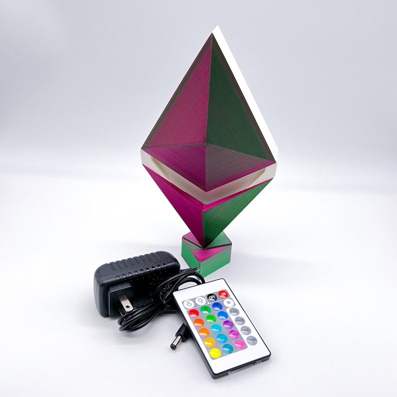 May include: A geometric, diamond-shaped lamp with a pink and green colour scheme. The lamp has a white light panel and comes with a remote control and a power adapter.
