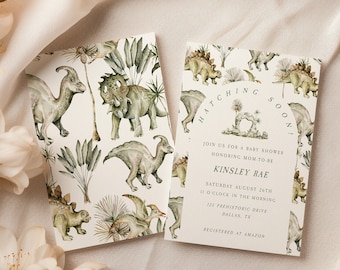 May include: A baby shower invitation with a dinosaur theme. The invitation is white with green watercolor dinosaurs and plants. The text reads "Hatching Soon!" and includes the baby's name, date, time, and location. The invitation also includes the text "Registered at Amazon."