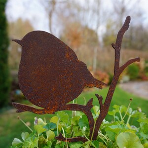 Könnte beinhalten: Rostbraune Metall-Vogel-Silhouette auf einem Ast, vor verschwommenem Grün. Diese dekorative Gartenverzierung verleiht Außenbereichen einen Hauch von Natur.