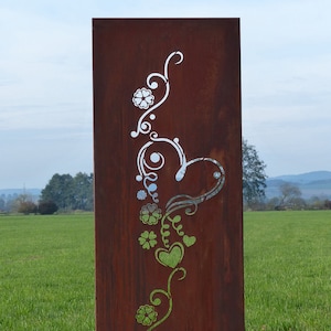 Könnte beinhalten: Ein rostiger Metall-Gartenschirm mit einem weißen Ausschnitt-Design aus einem Herzen, Blumen und Ranken. Der Schirm steht auf einer grasbewachsenen Wiese.