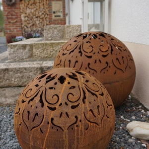 Puede incluir: Dos grandes esferas de metal oxidado con intrincados dise&ntilde;os recortados. Las esferas est&aacute;n sentadas sobre un lecho de peque&ntilde;as piedras grises.