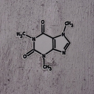 Könnte beinhalten: Ein schwarz-weißes chemisches Strukturdiagramm von Koffein, gedruckt auf einem weißen Aufkleber. Der Aufkleber ist etwa 4 x 5 Zentimeter groß.