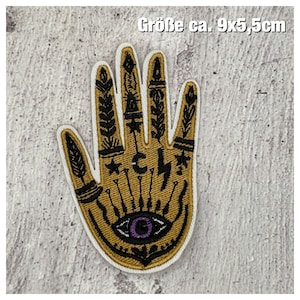 Könnte beinhalten: Ein gold gestickter Patch einer Hand mit einem allsehenden Auge und anderen Symbolen. Der Patch ist ca. 9 x 5,5 cm groß. "Größe ca. 9x5,5cm" steht in Deutsch oben im Bild.
