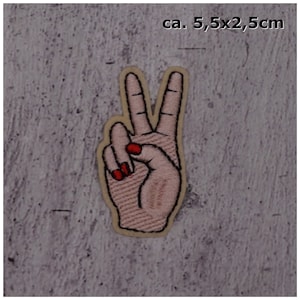 Könnte beinhalten: Gestickter Bügel-Patch mit einer rosa Hand, die das Friedenszeichen mit rotem Nagellack macht. Der Patch misst etwa 5,5 cm x 2,5 cm.