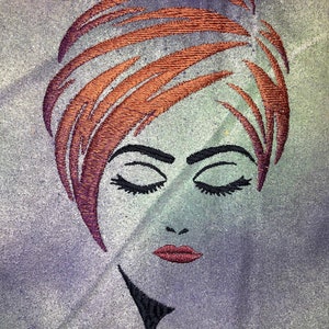 May include: Embroidered image of a woman with closed eyes and red lips. Her hair is styled in a short, layered bob and is a reddish-brown colour. The background is a muted purple and green.