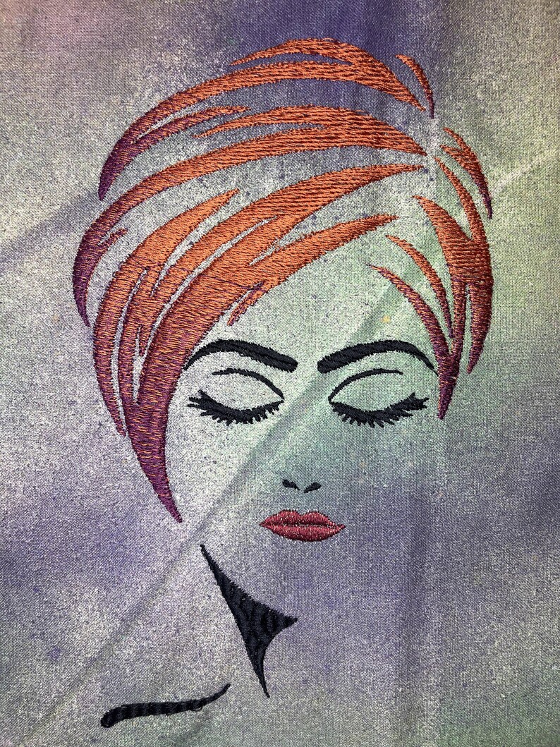 May include: Embroidered image of a woman with closed eyes and red lips. Her hair is styled in a short, layered bob and is a reddish-brown colour. The background is a muted purple and green.