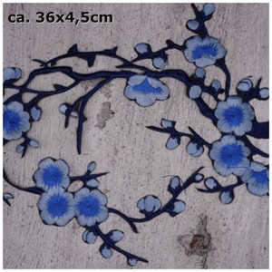 Könnte beinhalten: Blau-grauer gestickter Blumenapplikation-Patch, ca. 36 x 4,5 Zentimeter groß. Der Patch zeigt einen stilisierten Zweig mit zarten Blüten und Blättern.