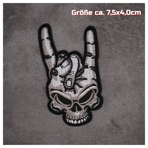 Könnte beinhalten: Ein gestickter Patch in Schwarzweiß mit einer Skeletthand, die das Rock'n'Roll-Handzeichen macht. Der Patch ist etwa 7,5 cm x 4 cm groß.