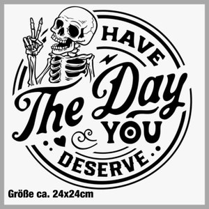 Könnte beinhalten: Schwarz-weiß-Illustration eines Skeletts mit einem Peace-Zeichen, in einem Kreis mit dem Text "Have the Day You Deserve". Das Bild ist etwa 24 cm x 24 cm groß.