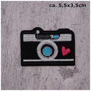Könnte beinhalten: Schwarz-weiß gestickter Bügel-Patch einer Kamera mit blauem Objektiv und rotem Herz. Der Patch misst etwa 5,5 cm x 3,5 cm.