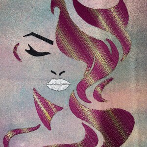 May include: Embroidered design of a woman's face with pink and gold hair. The woman's eyes are closed and her lips are slightly parted. The background is a light blue and pink watercolour wash.