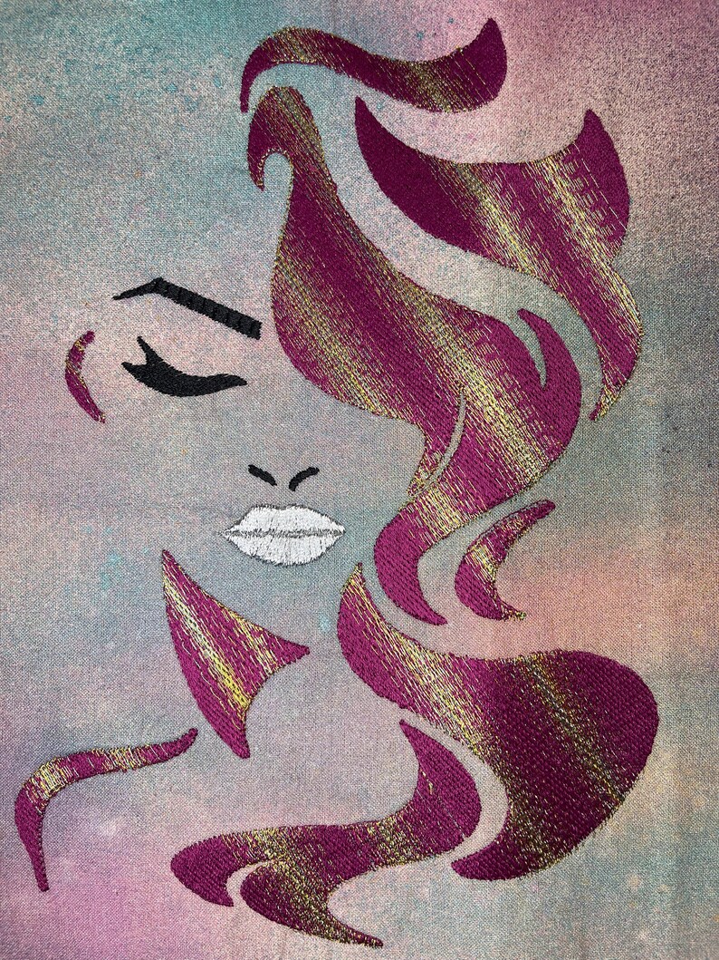 May include: Embroidered design of a woman's face with pink and gold hair. The woman's eyes are closed and her lips are slightly parted. The background is a light blue and pink watercolour wash.