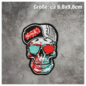 Könnte beinhalten: Gestickter Bügel-Patch mit einem Totenkopf, der eine Sonnenbrille und eine Baseballkappe mit dem Wort "aint" trägt. Der Totenkopf ist rot, weiß und blau. Der Patch ist etwa 6,8 x 9,8 Zentimeter groß.