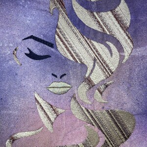 May include: A stylised embroidered image of a woman's face with a purple and pink background. The woman's hair is a gold and brown striped pattern.