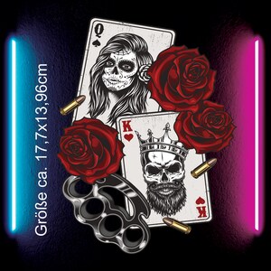 Könnte beinhalten: Zwei Spielkarten, eine Dame Pik und ein König Herz, mit einem Totenkopf und Bart auf der Königskarte. Die Karten sind von roten Rosen und Kugeln umgeben. Ein silberner Schlagring befindet sich im Vordergrund. Der Text "Größe ca. 17,7x13,96cm" befindet sich auf der linken Seite des Bildes.