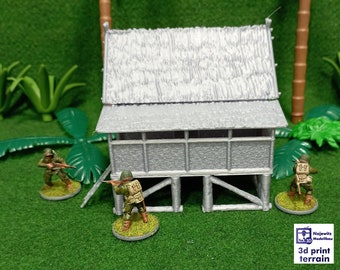 May include: A gray, wooden, miniature building with a thatched roof, surrounded by green foliage and three miniature figures holding rifles. The building has a porch and a wooden frame. The figures are wearing green uniforms and are standing on small bases.