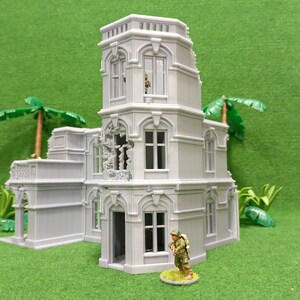 May include: A gray, detailed, multi-level, ruined building model with a small figure standing in front of it. The building has a tower with a window and a balcony. The building is on a green surface.