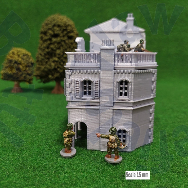 Puede incluir: Un edificio en miniatura gris, impreso en 3D, con soldados en el tejado y en el suelo. El edificio tiene ventanas detalladas y un balc&oacute;n. El texto "Scale 15 mm" es visible. El fondo presenta &aacute;rboles en miniatura y una superficie verde.