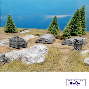 May include: A collection of miniature grey 3D-printed terrain pieces, including a multi-storey building, two arched structures, and a watchtower, are displayed on a diorama with miniature trees and rocks. The background is a blue sky.