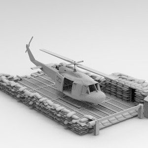 Könnte beinhalten: Ein graues Modell eines Hubschraubers, der auf einer Holzplattform landet, die von Sandsäcken umgeben ist. Die Plattform ist von einem Zaun umgeben.