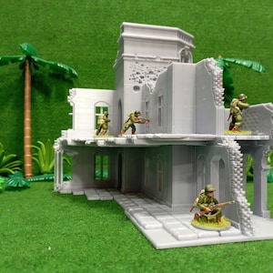 May include: A gray, ruined building with a tower, partially destroyed, with four miniature figures in military uniforms standing on the roof and inside the building. The building is set against a green background.