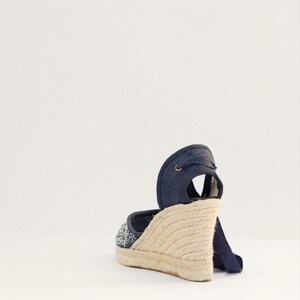 Op de afbeelding: Een spijkerblauwe espadrille sandaal met een geweven jute zool. De sandaal heeft een wikkelenkelband en een decoratief patroon op de teen. De sleehak meet ongeveer 7.6 cm.
