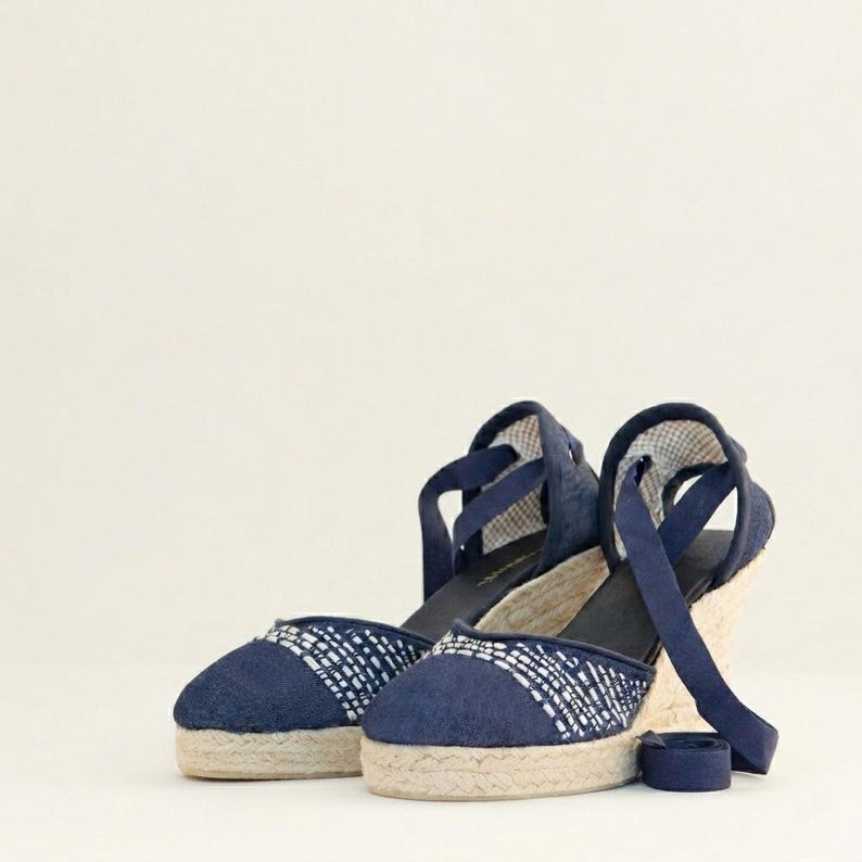 Op de afbeelding: Een paar marineblauwe espadrille sandalen met sleehak. De sandalen hebben een geweven jute zool, een marineblauwe stoffen bovenkant met een wit patroon en enkelbanden. De sleehak biedt een comfortabele lift.
