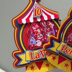K&ouml;nnte beinhalten: Ein farbenfroher Tortenaufsatz im Zirkus-Design mit der Zahl 10. Das Design zeigt ein rot-wei&szlig; gestreiftes Zelt, Cartoon-Figuren und den Namen "Lavi" auf einem Banner. Der Aufsatz ist mit roten, gelben und blauen Akzenten versehen.