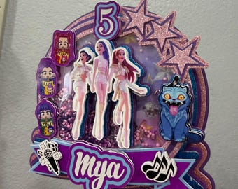 May include: A layered cake topper featuring the number 5, three cartoon figures, a blue cat, and the name Mya on a purple banner. The design includes pink glitter stars, a microphone icon, musical notes, and a shaker element filled with purple beads.