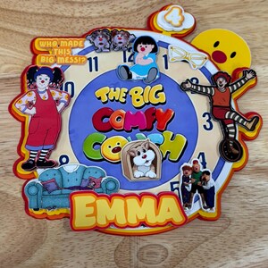 Pode incluir: Um rel&oacute;gio de parede circular com o tema The Big Comfy Couch, mostrador azul, n&uacute;meros pretos e recortes de personagens coloridos. O texto diz Who Made This Big Mess, The Big Comfy Couch e o nome Emma em letras amarelas na parte inferior.