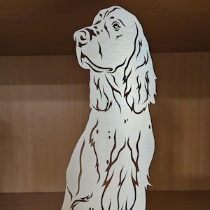 Könnte beinhalten: Ein silberner Metall-Buchstütze in Form eines sitzenden Hundes. Der Hund blickt nach rechts und hat einen langen, fließenden Schwanz.