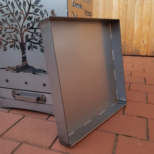 May include: A metal fire pit with a tree design cut out. The fire pit has a removable metal grate. The fire pit is sitting on a brick patio.
