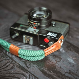 Op de afbeelding: Een zwarte en zilveren 35mm filmcamera met een groene en bruine cameraband. De camera heeft een rode knop en de tekst "400 SE PRIME" aan de zijkant.