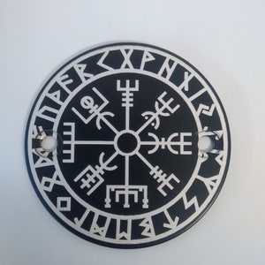 Op de afbeelding: Een zwarte ronde kompas met een wit ontwerp. Het kompas heeft een traditionele kompasroos met vier windrichtingen en een cirkel van runen rond de rand.