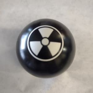 Peut inclure: Une sphère noire avec un symbole de radiation blanc imprimé dessus.