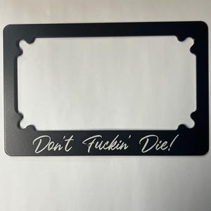 May include: Black metal license plate frame with the text "Don't Fuckin' Die!" in white lettering.
