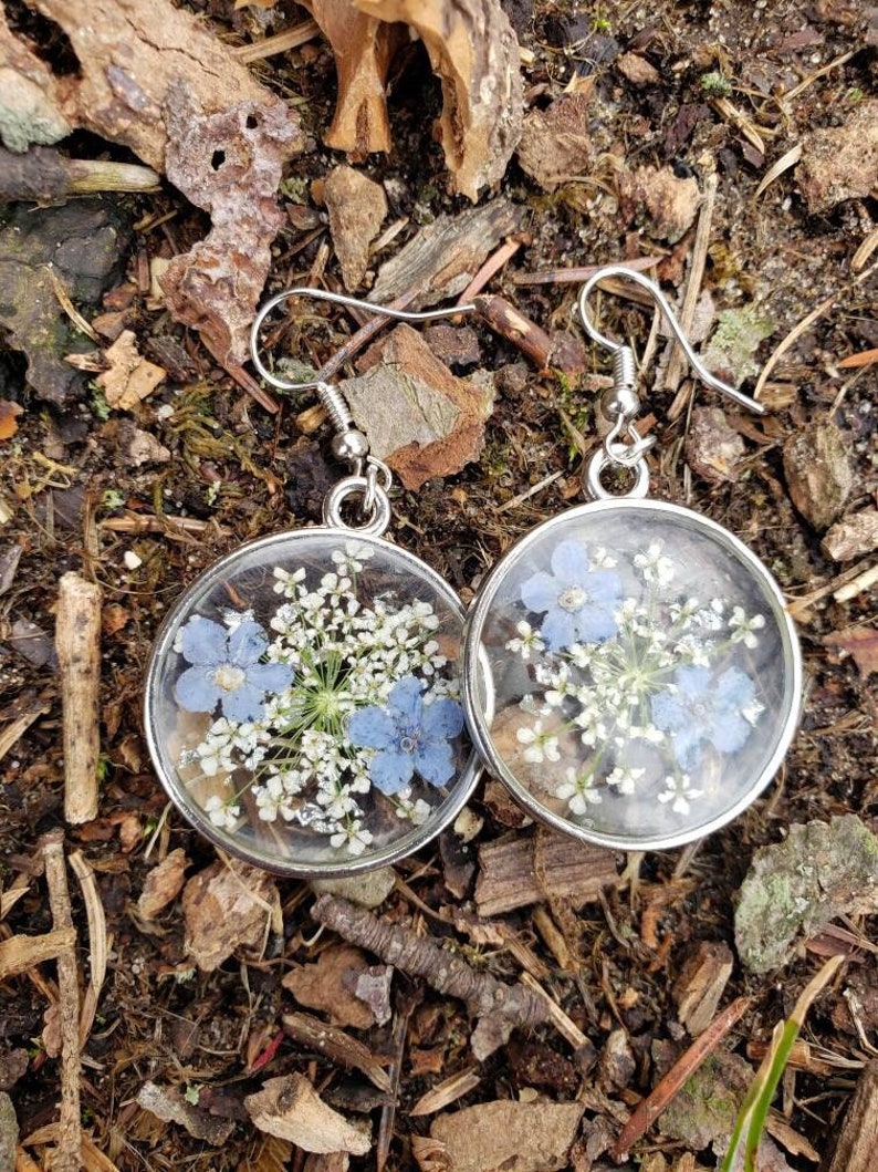 May include: A pair of silver earrings with clear resin and pressed flowers. The flowers are white and blue.