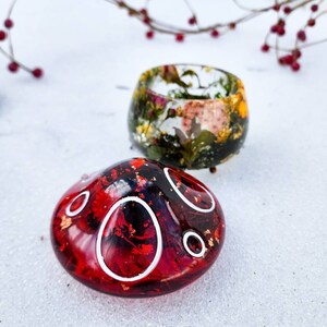 May include: Two resin trinket dishes, one red with white circles and one with a floral design in shades of green, brown, and white.