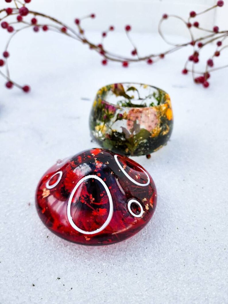 May include: Two resin trinket dishes, one red with white circles and one with a floral design in shades of green, brown, and white.