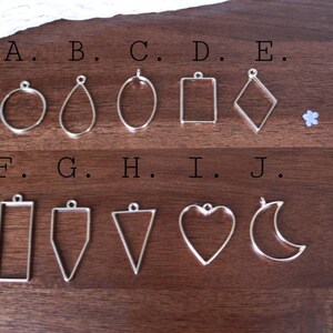 May include: Ten silver metal pendant blanks in various shapes, labeled A through J. The shapes include a circle, teardrop, oval, square, diamond, rectangle, triangle, heart, and crescent moon.