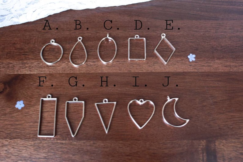 May include: Ten silver metal pendant blanks in various shapes, labeled A through J. The shapes include a circle, teardrop, oval, square, diamond, rectangle, triangle, heart, and crescent moon.