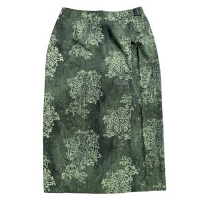 May include: A midi-length skirt in a deep olive green shade featuring a repeating light green damask-style pattern. The garment has a wrap-front design with a single dark rectangular buckle closure located at the right side of the waistband.