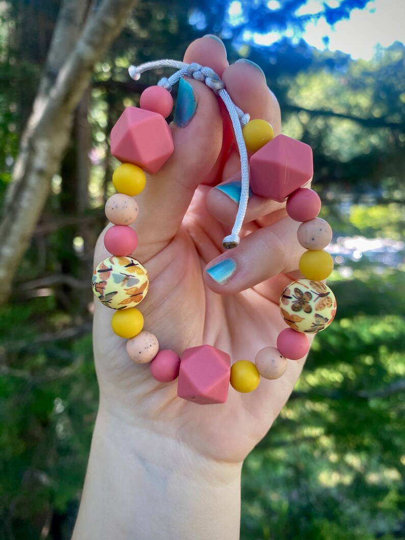 May include: A pink and yellow silicone bracelet with a variety of beads, including some with a leaf pattern.