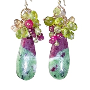 May include: A pair of dangle earrings featuring green and pink gemstones. The earrings have a teardrop-shaped green and pink stone with smaller green and pink gemstones clustered around the top.