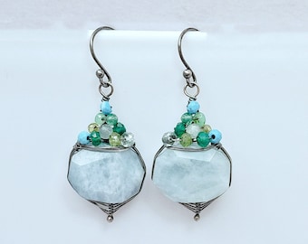 May include: A pair of silver earrings featuring a light blue gemstone and a cluster of green and blue beads.