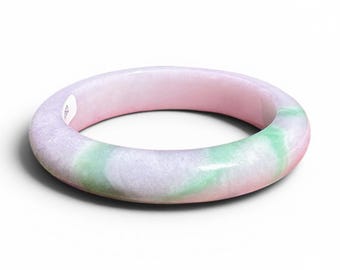 May include: A jade bangle bracelet with a smooth, rounded design. The bracelet displays a mix of pink, green, and white hues. The polished surface reflects light, accentuating the natural patterns of the stone. A classic piece of jewellery.