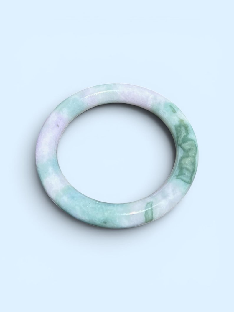 May include: A smooth, circular bangle bracelet crafted from polished stone, featuring a marbled pattern with soft lavender and light green hues blended throughout the material, creating a continuous, solid, and rounded band design.