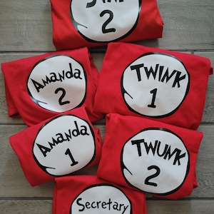 May include: Six red t-shirts with white circles and black text. The text on the shirts reads "Jim 2", "Amanda 2", "Amanda 1", "Twink 1", "Twink 2", and "Secretary 1".