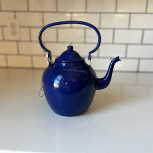 Op de afbeelding: Een blauwe emaille theepot met een zilveren ketting en een deksel. De theepot heeft een handvat en een tuit.
